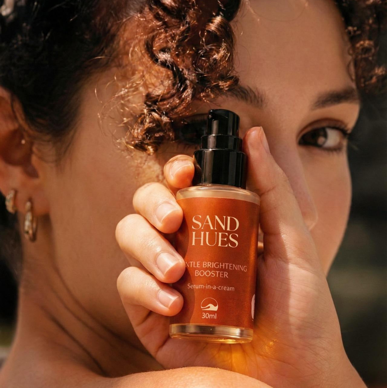 Person holding a 'Sand Hues' skincare product close to their face